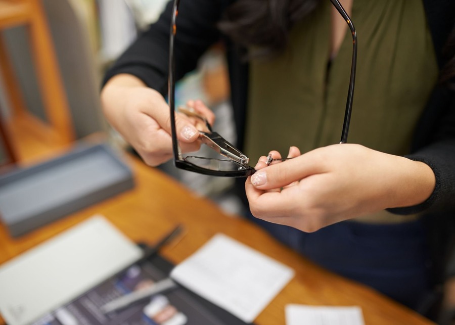 A designer using calipers to meticulously measure an eyewear sample against a technical drawing.